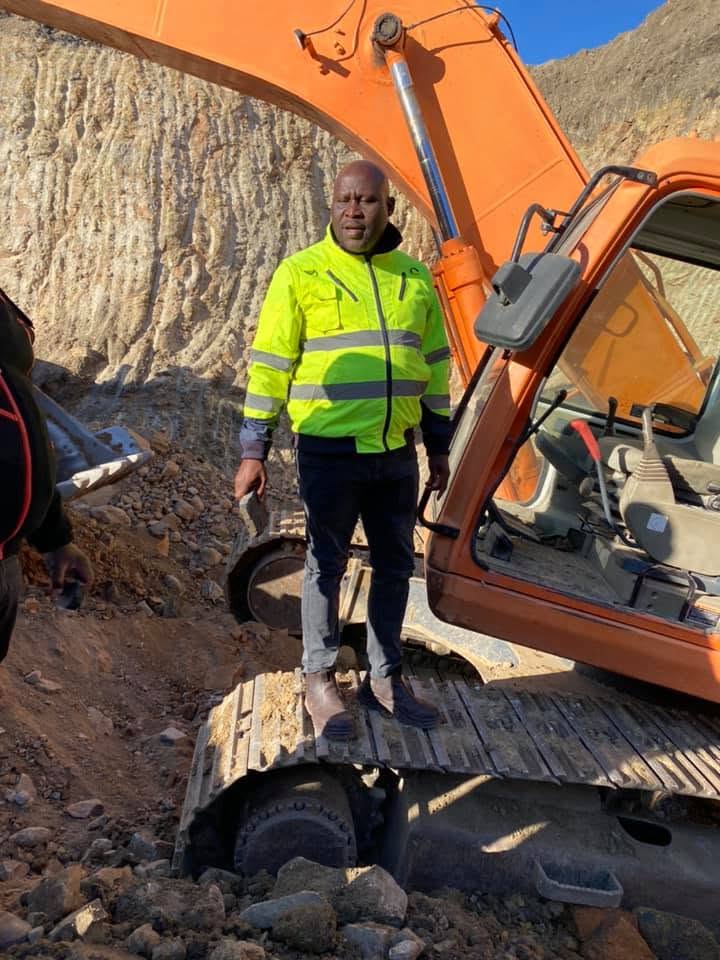 Person in high-visibility clothing beside an orange excavator at an earthworks site